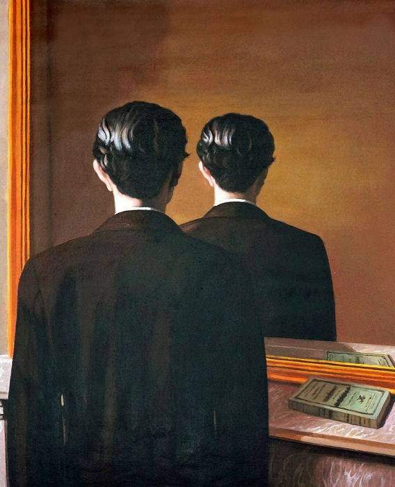 Two men in dark suits stand with their backs to the camera, facing a warm wall and a large mirror.